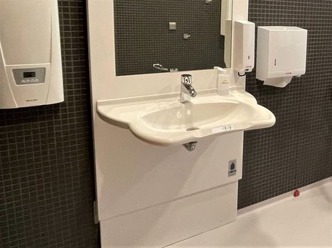 Auf einer höhenverstellbaren Grundplatte ist ein Waschtisch mit Spiegel und Seifenspender montiert. An der Vorderseite des Waschtisches befinden sich Bedienknöpfe zur Höhenverstellung.