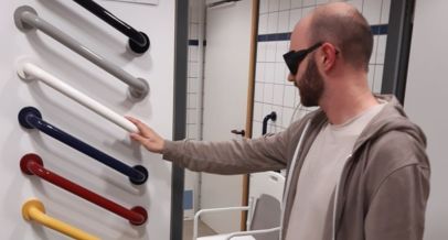 Mann mit einer Simulationsbrille für Sehbeeinträchtigungen erprobt Haltegriffe mit und ohne Kontrast zur Wand