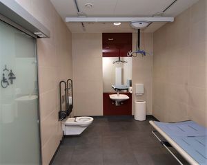 Gesamtansicht einer Toilette für alle. Zusätzlich zum barrierefreien WC und Waschtisch gibt es eine höhenverstellbare Liege und einen in zwei Richtungen verschiebbaren Personenlifter an der Decke.