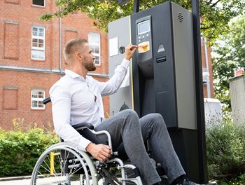 Foto eines Rollstuhlfahrers an einem barrierefreien Parkticket-Automaten