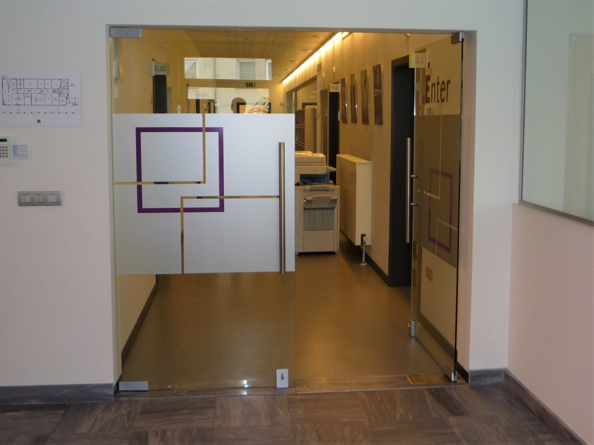 Foto von einer Glastür, die in einen Büroflur führt. Die Glastür ist durch weiße und lilafarbene Glasmarkierungen deutlich erkennbar.